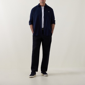 Model wearing Lacoste navy blue cotton casual shirt with small crocodile logo, styled with black trousers and navy canvas trainers