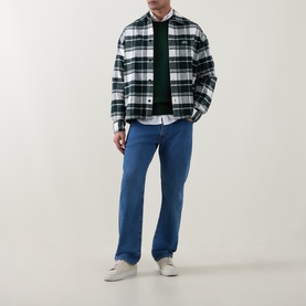 Model wearing Lacoste Flour check casual shirt in white and green plaid, styled with green knit, blue straight-leg jeans and white trainers