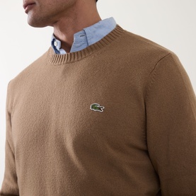 Model wearing Lacoste wool crew neck jumper in cookie brown with signature crocodile logo, styled with light blue collared shirt underneath