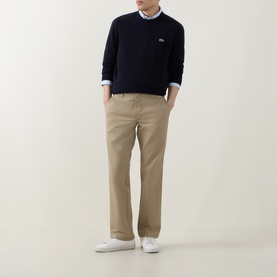 Model wearing Lacoste Navy Blue wool crew neck jumper with beige chinos and white trainers.