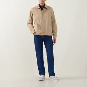 Model wearing Lacoste Viennese cotton overshirt in beige, styled with dark blue jeans and white trainers.