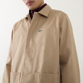 Model wearing Lacoste Overshirt in Viennese beige cotton, with iconic crocodile logo, styled over a dark collared shirt.