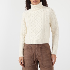 Model wearing Nili Lotan ivory lambswool cable-knit turtleneck sweater, styled with brown wide-leg trousers.