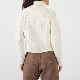 Model wearing Nili Lotan ivory lambswool cable-knit turtleneck sweater, back view, styled with brown trousers.