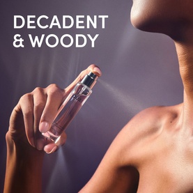 Model holding Ouai EDP fragrance bottle, spraying mist, with Decadent & Woody text overlay visible