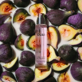 Ouai EDP in a pink glass bottle with silver cap, surrounded by fresh purple figs and fig halves on a white surface