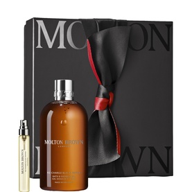 Molton Brown bath and body gift set with black ribbon-tied box, amber bath gel bottle, and travel-size spray