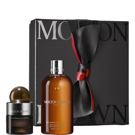 Molton Brown fragrance gift set with black bow-tied box, amber glass bottle, and travel-size candle