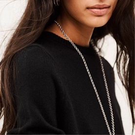 Model with long silver chain necklace and hoop earrings, styled with a black knit jumper
