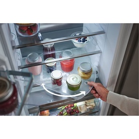 Miele Built-in 70/30 Fridge-Freezer interior with rotating lazy Susan shelf, hand accessing food items on glass shelves