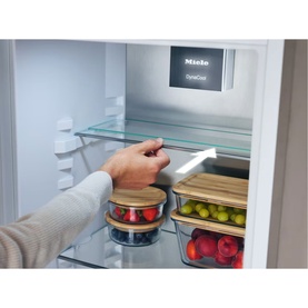 Miele Built-in 70/30 Fridge-Freezer interior showing PerfectFresh Active drawer with hand pulling glass shelf, fresh produce stored in containers.