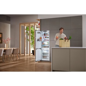 Miele Built-in 70/30 Fridge-Freezer open in a modern kitchen, showing interior storage, with a person unloading groceries nearby.