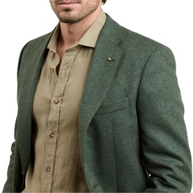 Model wearing Magee 1866 green blazer with small lapel pin, styled with a beige linen shirt.