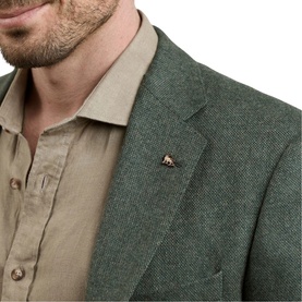Magee 1866 green tweed blazer detail shot showing lapel pin emblem, worn over a beige linen shirt