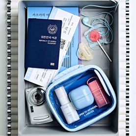 Laneige Beauty All Skincare Set in blue travel pouch, styled in a suitcase with passport, boarding pass, and camera