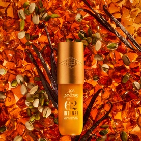 Sol De Janeiro Cheirosa 62 Intense Perfume Mist in gold bottle, surrounded by amber resin pieces, vanilla pods and seeds on orange background