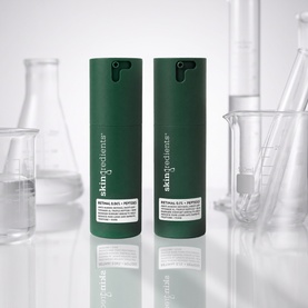 The Skin Nerd Retinal .06% + Peptides serum in dark green pump bottles, shown as a duo against a laboratory backdrop