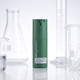 The Skin Nerd Retinal .06% + Peptides serum in dark green pump bottle, styled among glass lab beakers and flasks
