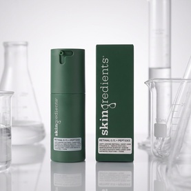 The Skin Nerd Retinal .06% + Peptides serum in dark green pump bottle beside its box, styled with laboratory glassware