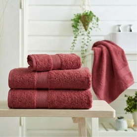 Deyongs Plain Raspberry towels stacked on wooden bench, with hand towel draped over bath edge in bright bathroom setting