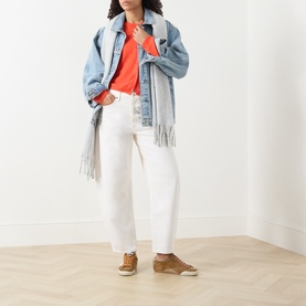 Model wearing American Vintage coral knitwear, styled with oversized denim jacket, grey fringed scarf, white jeans and tan flat shoes.
