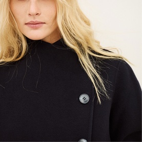 Model wearing Bash blue coat, close-up detail of dark buttons and funnel neckline