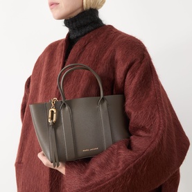 Model carrying Marc Jacobs The Small Work Tote Bag in Forest pebbled leather, gold-tone hardware, dual top handles, styled with rust knit coat