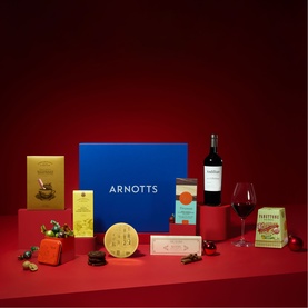 Arnotts Food Retail Hamper with blue gift box, red wine bottle, wine glass, chocolates, biscuits, and festive food items on red background