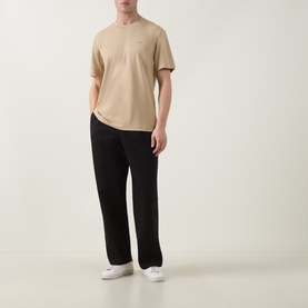 Model wearing Lacoste beige crew neck T-shirt in 100% cotton, styled with black wide-leg trousers and white trainers.