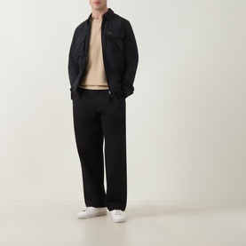 Model wearing Lacoste Beige Crew Neck T-Shirt, styled with black overshirt, wide-leg black trousers and white trainers.