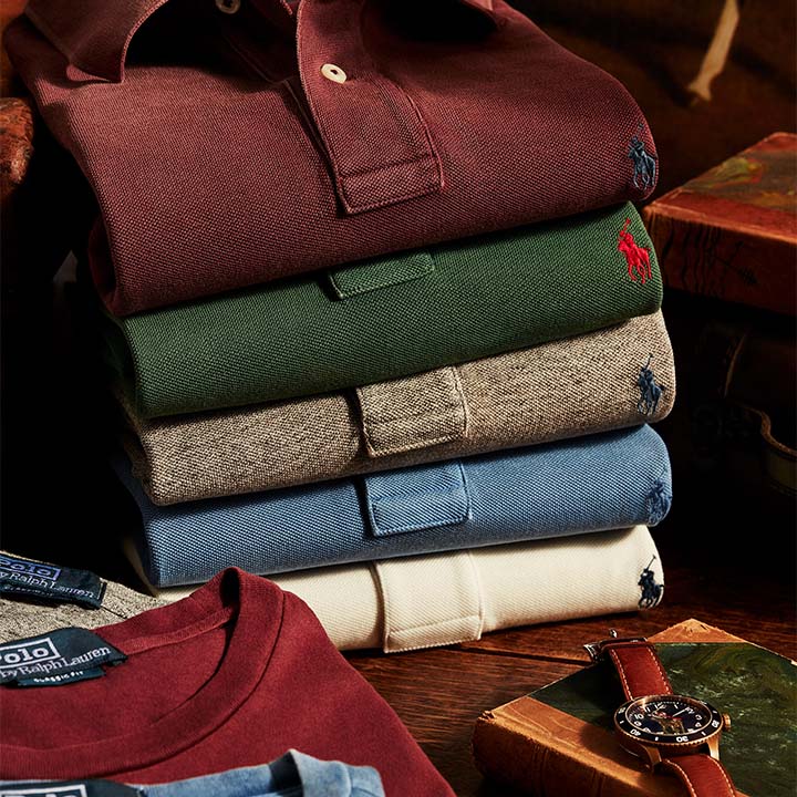 A stack of neatly folded polo shirts in various colors sits on a wooden table beside a wristwatch.