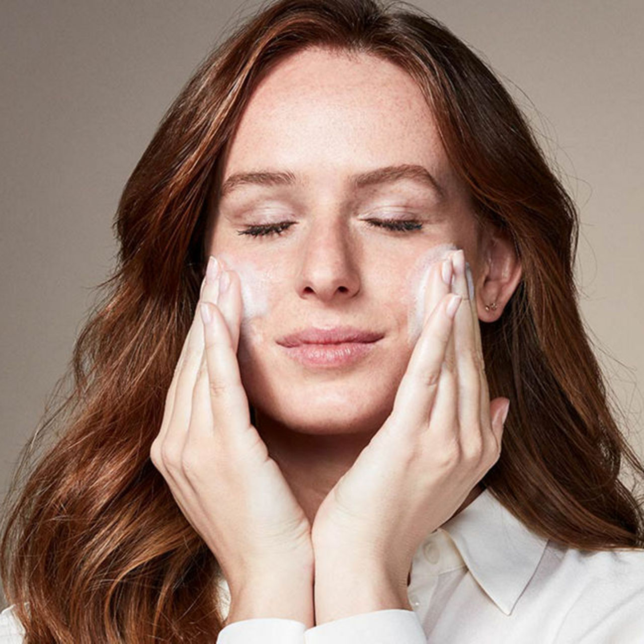 Woman with closed eyes applying facial cleanser to face, hands cupping cheeks, using The Ritual of Namasté Purify product.
