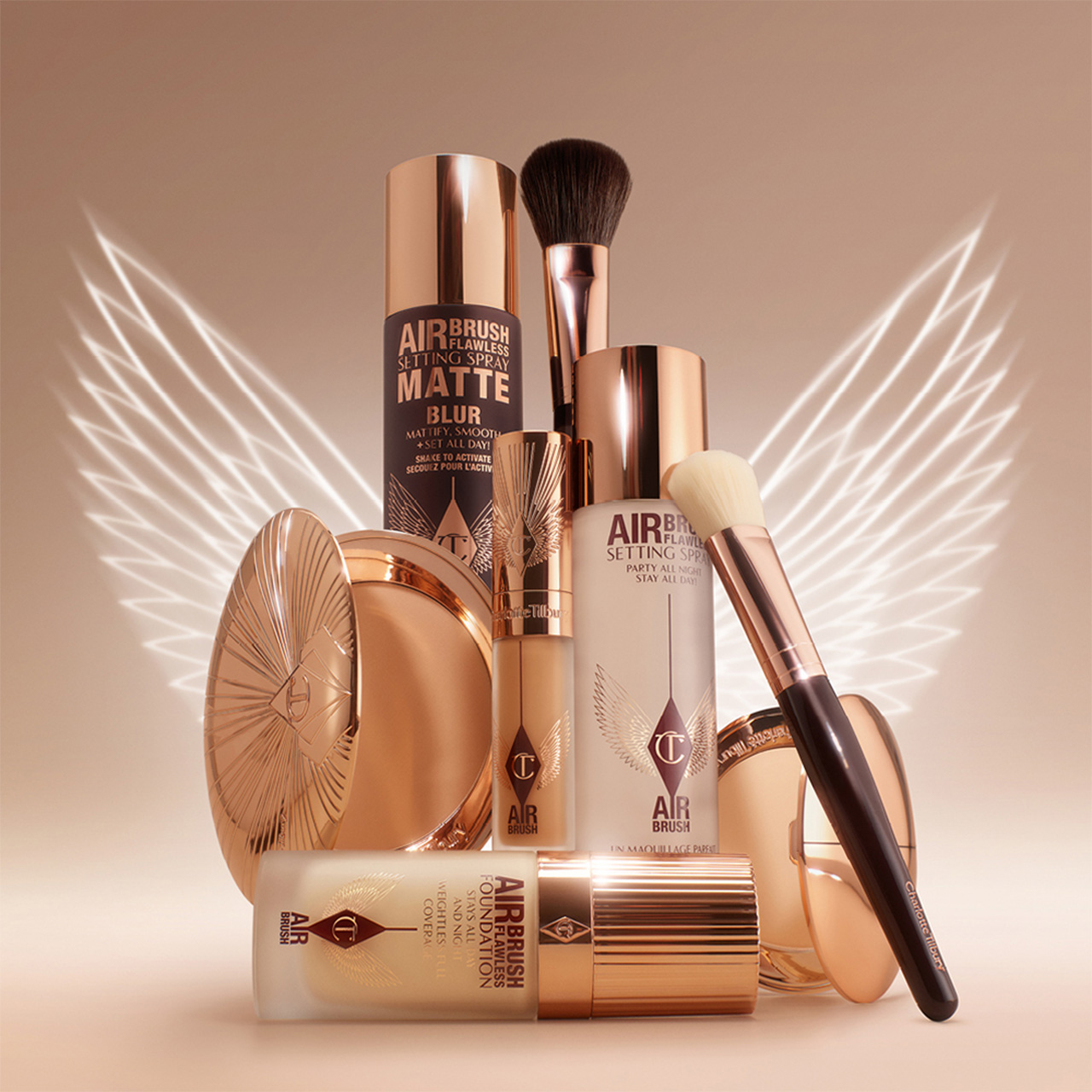 Complexion makeup collection featuring airbrush setting sprays, foundation, brushes, and powder compacts arranged with decorative wings on neutral background