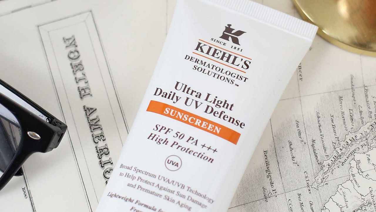 Kiehl's Ultra Light Daily UV Defense sunscreen lying on an open map with black sunglasses to the left side