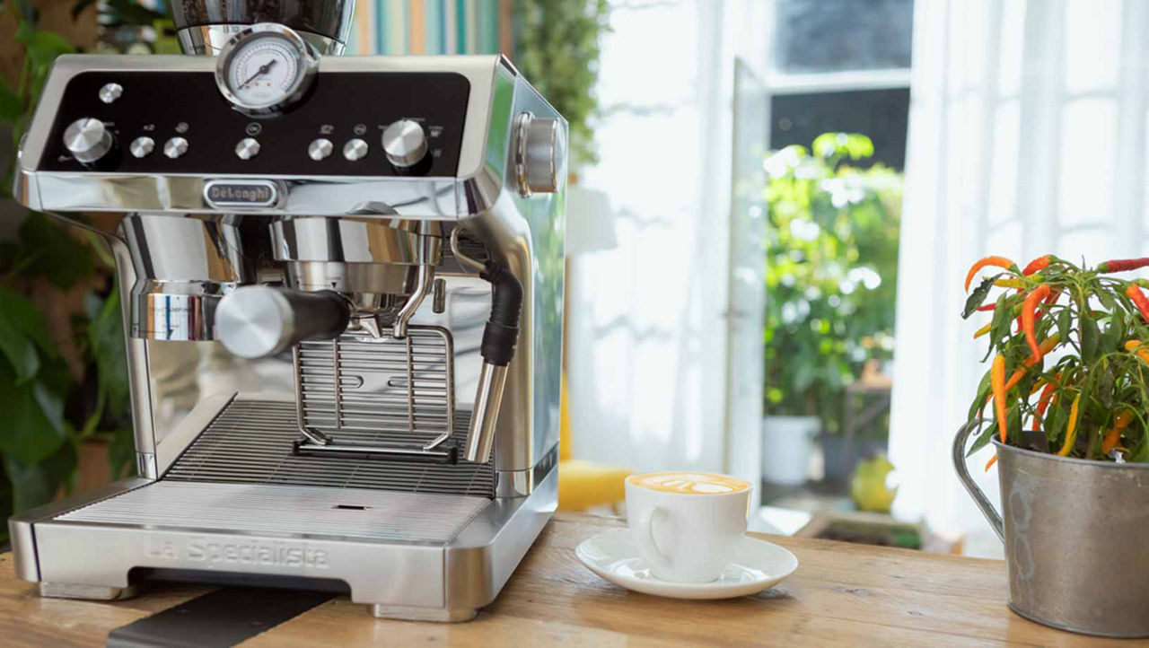 Steel coffee machine on a wooden bench with a full coffee cup beside it.