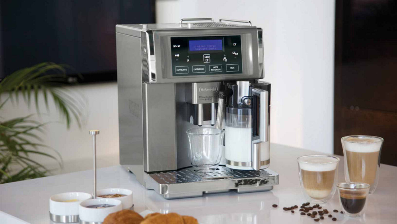 Silver coffee machine on a marble counter top. Various cups of different types of coffee sit on the counter around it with some coffee beans spilt beside them.