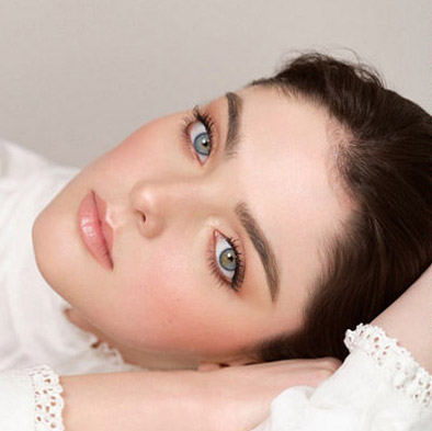 Person with light blue eyes and flawless skin lying on their arm, wearing a white top.