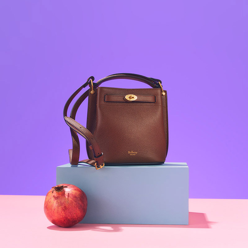 A colorful display of bags, skincare products, a teapot, cosmetics, a plush toy, a watch, and a pomegranate, arranged on pastel blocks.