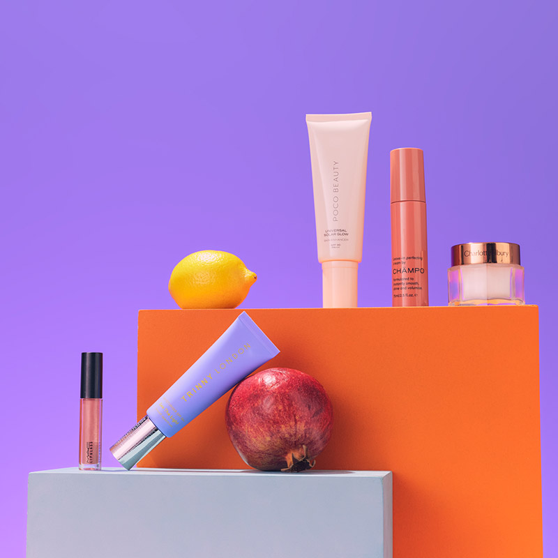 Cosmetic products displayed with a lemon and apple against a purple background.