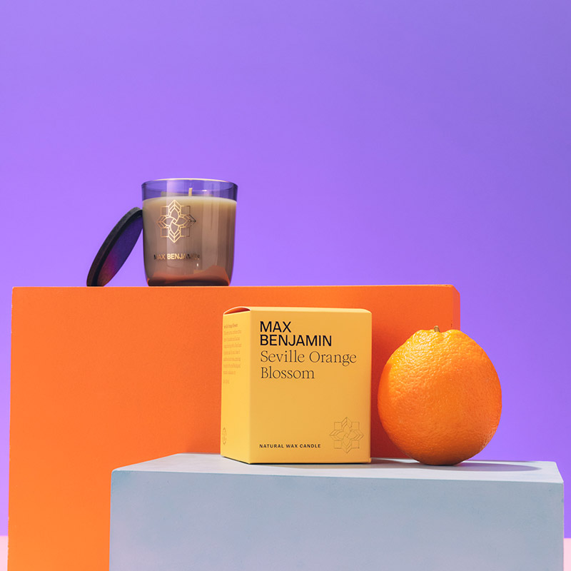 Candle, orange box, and an orange on colorful blocks against a purple background.