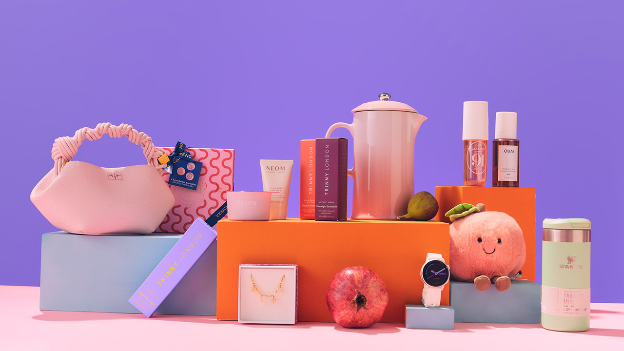 A colorful display of bags, skincare products, a teapot, cosmetics, a plush toy, a watch, and a pomegranate, arranged on pastel blocks.