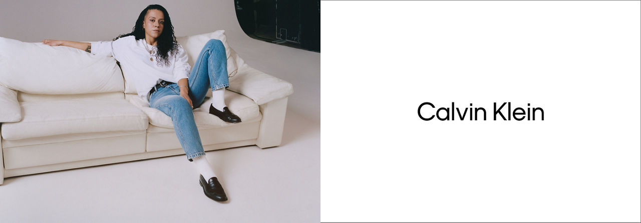 Woman on cream couch wearing blue CK Jeans and white sweatshirt with Calvin Klein logo