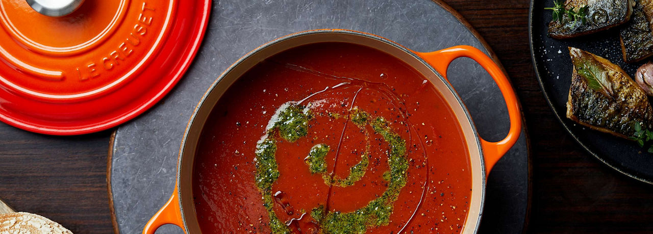 Orange and red Le crueset pot with tomato soup and pesto