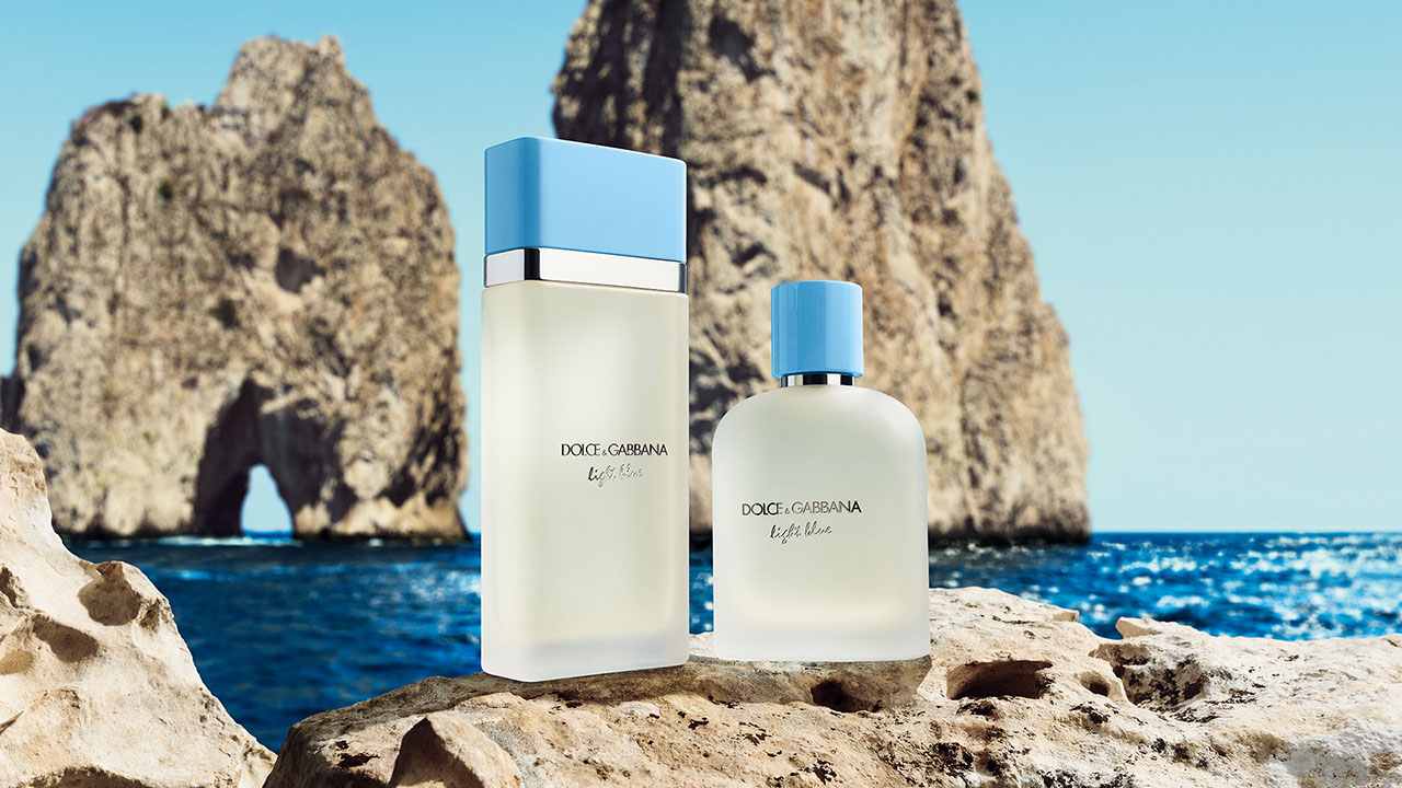 
Two Dolce & Gabbana Light Blue perfume bottles are displayed on rocks with a scenic sea and cliff backdrop.

