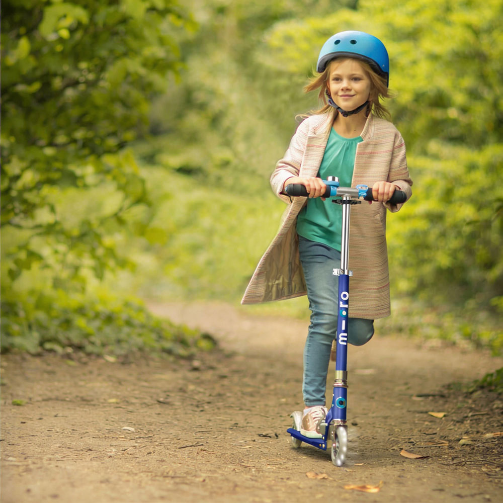 A child in a blue helmet rides a blue scooter on a forest path. 