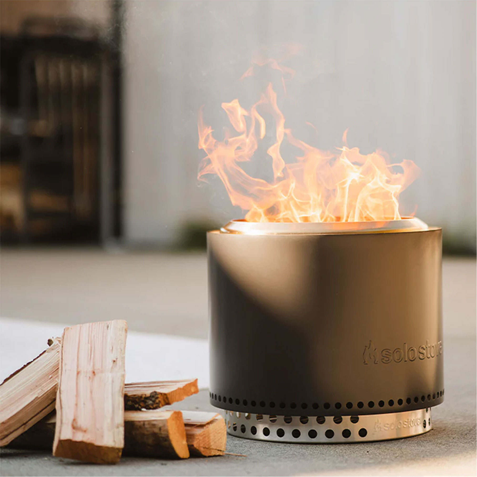 A smokeless fire pit with bright flames, surrounded by pieces of stacked firewood.