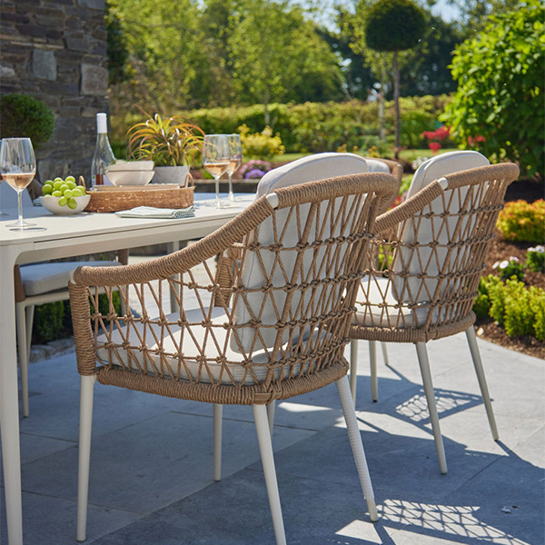 Outdoor dining setup with wicker chairs and a table set with wine and food, surrounded by greenery.