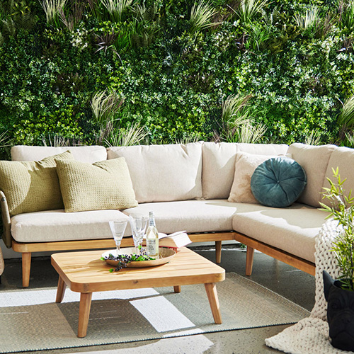 A cozy outdoor seating area with a beige sectional sofa, wooden coffee table, and lush vertical garden.