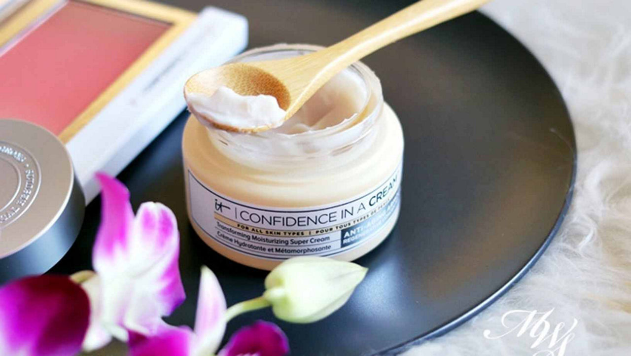 Confidence in a Cream by It cosmetics sitting open on a black plate with a small wooden spoon on top with product on it