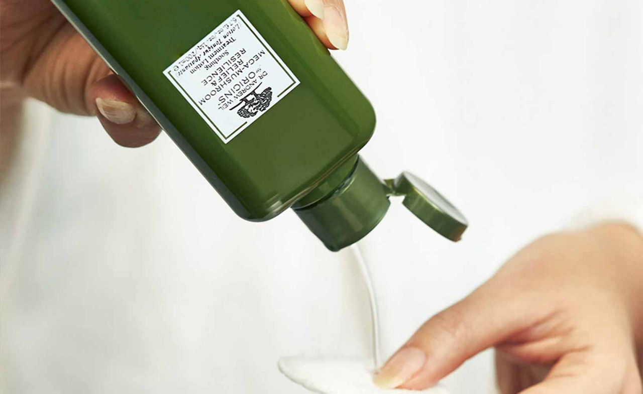 Origins Skin Toner bottle, held upside down by a woman squeezing product out onto a cotton pad